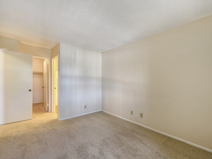 Empty apartment bedroom with white walls and plush carpeting through out.